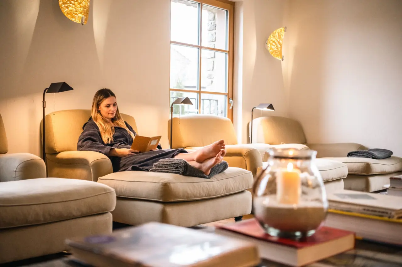 Gemütlicher Ruheraum im BollAnts Spa im Park: Frau im Bademantel entspannt lesend bei warmem Kerzenschein.