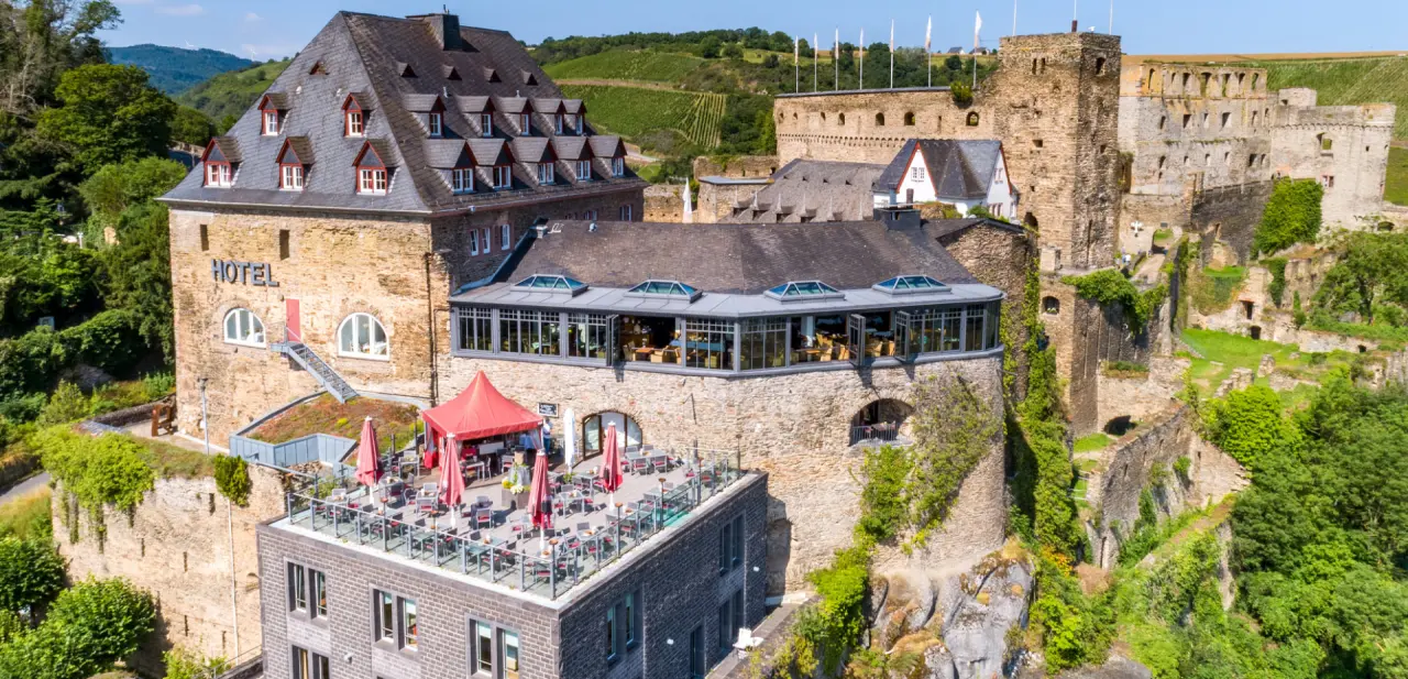 Historisches Hotel Schloss Rheinfels mit Restaurant, Dachterrasse und Blick auf die Burgruine und Weinberge am Rhein.
