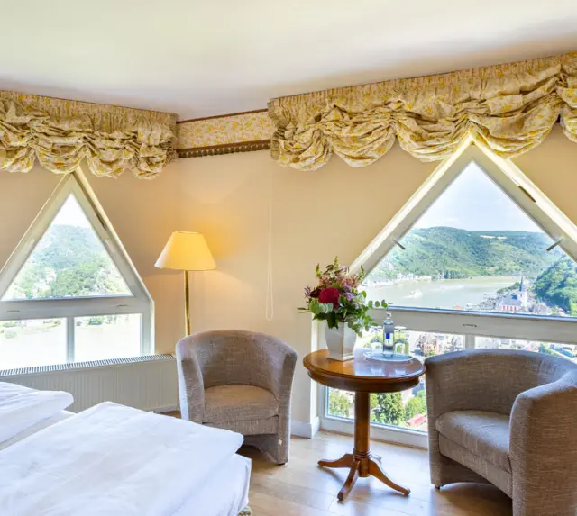 Gemütliches Hotelzimmer im Hotel Schloss Rheinfels mit einzigartigen dreieckigen Fenstern und Panoramablick auf den Rhein.