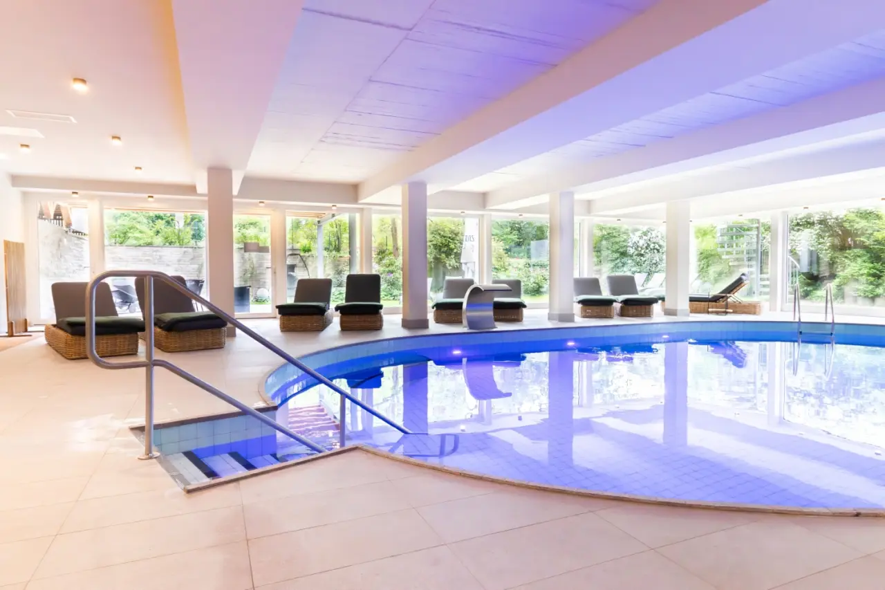Beheizter Innenpool mit Entspannungsliegen und Blick ins Grüne im Wellnessbereich des Hotel Ascona.