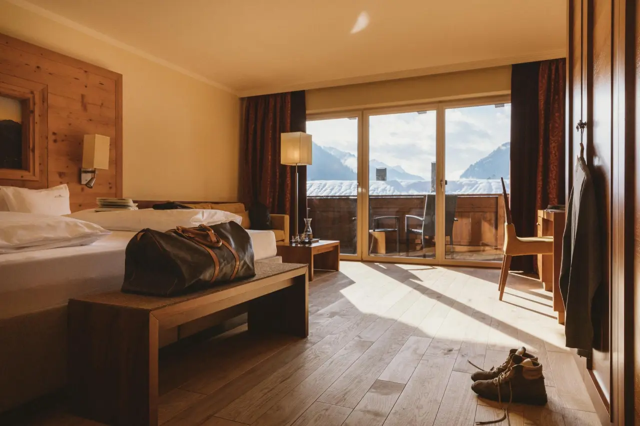 Gemütliches Hotelzimmer im Gartenhotel Linde mit Holzelementen, Balkon und Panoramablick auf die verschneiten Berge.