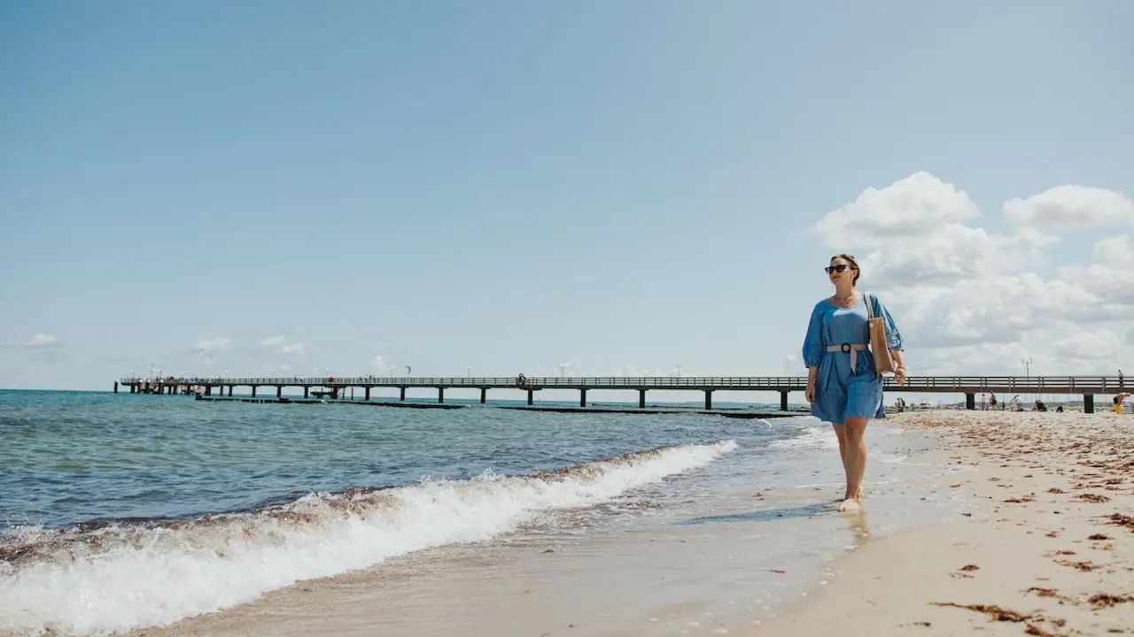 Frau spaziert am Strand von Kühlungsborn mit Seebrücke im Hintergrund. Entspannung nahe Hotel Vier Jahreszeiten.