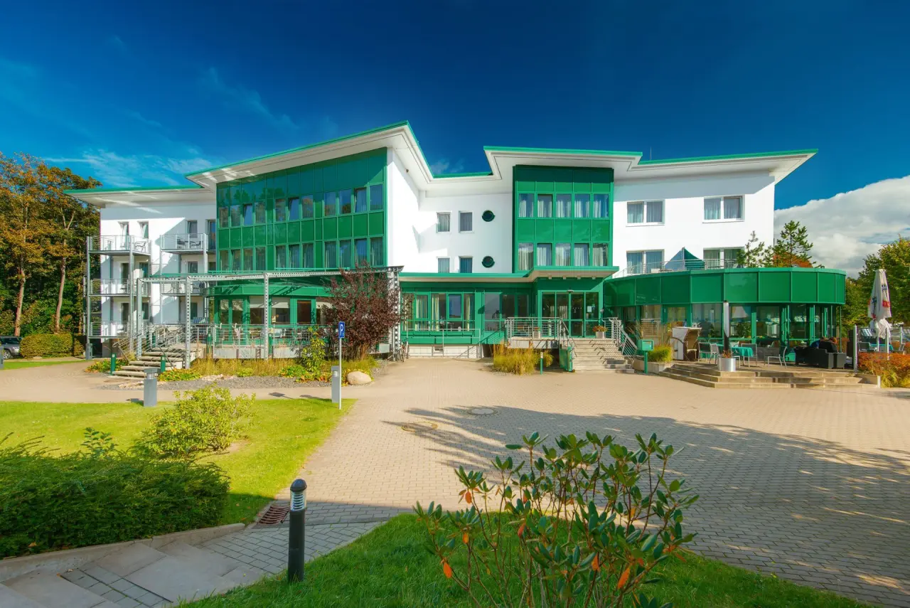 Moderne Aussenansicht des Hotel Vier Jahreszeiten Kühlungsborn unter blauem Himmel mit grünen Fassadenelementen und Terrasse.