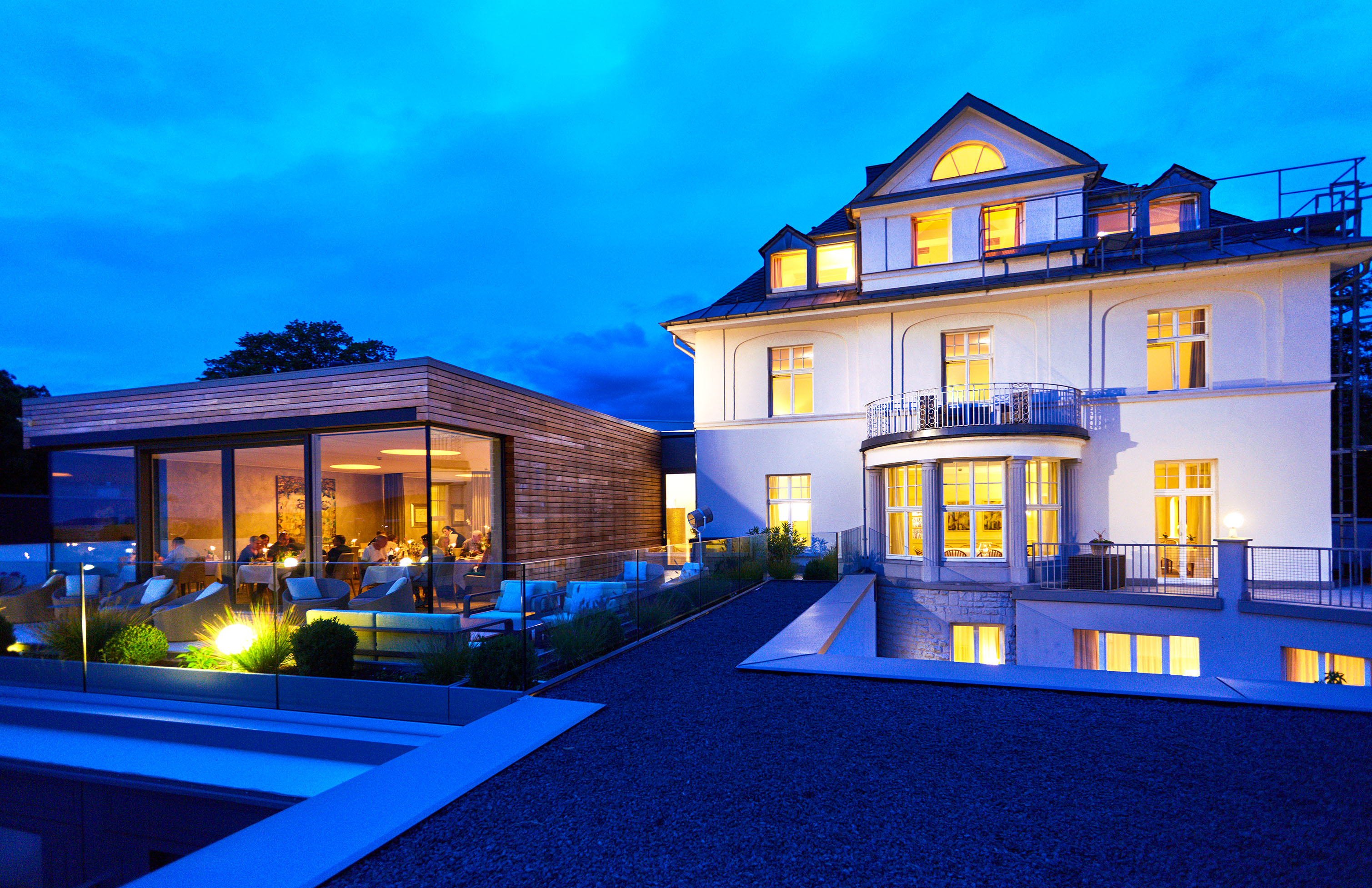 Hotel Villa Hügel in Trier – Hotelgebäude mit beleuchteter Terrasse und Restaurant bei Nacht | Wellnesshotel Mosel