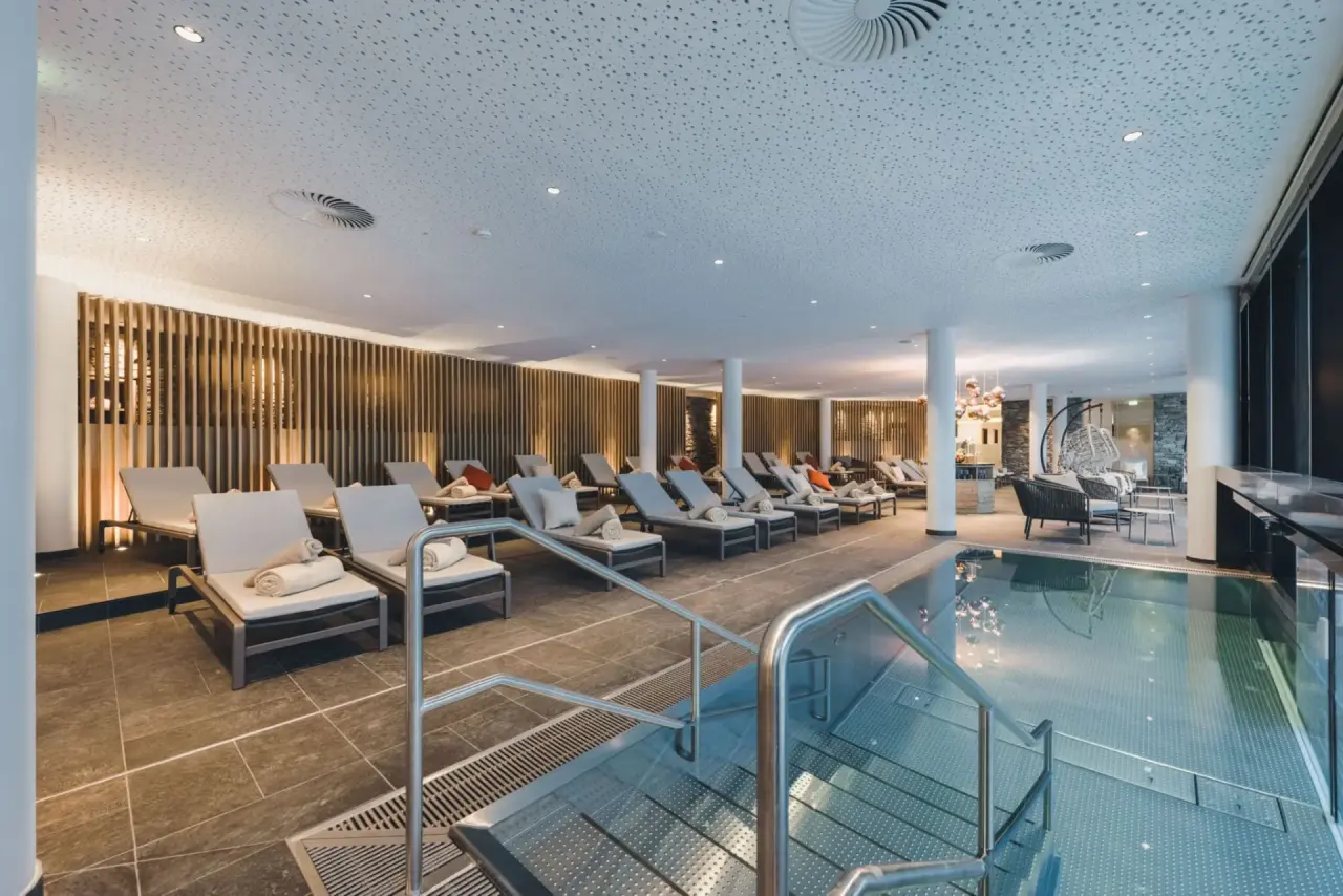 Grosszügiger Innenpoolbereich mit bequemen Liegestühlen und stilvollem Design im Alpenhotel Montafon.