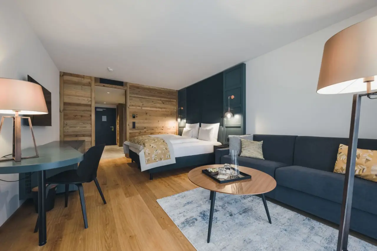 Geräumiges Hotelzimmer im Alpenhotel Montafon mit Doppelbett, Sofa, Schreibtisch und moderner Einrichtung.