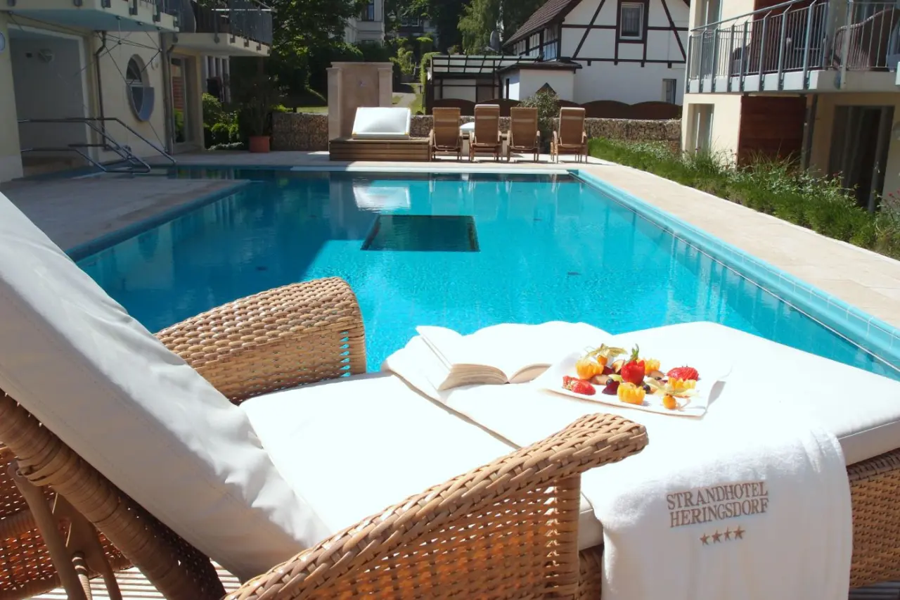 Aussenpool des Strandhotel Heringsdorf mit Sonnenliegen, frischen Fruechten und einem Buch fuer entspannte Stunden.