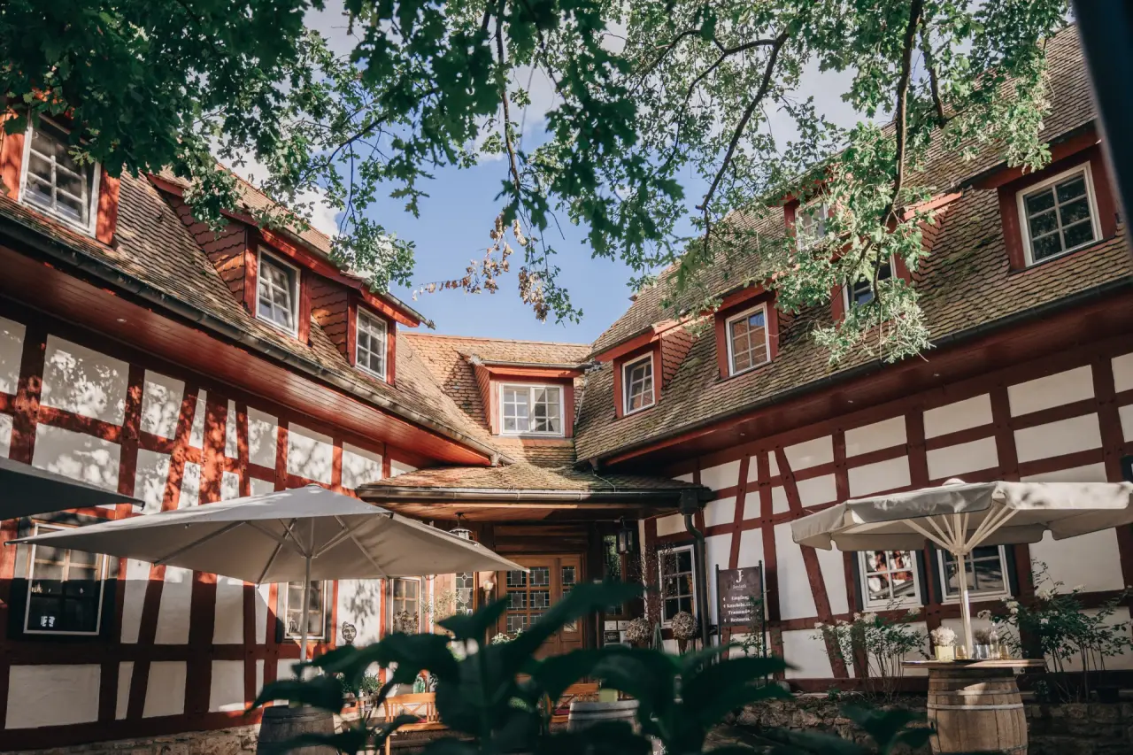 Historisches Fachwerkgebäude des Hotel Jordan's Untermühle mit grünen Bäumen und Außenterrasse im Sonnenlicht.
