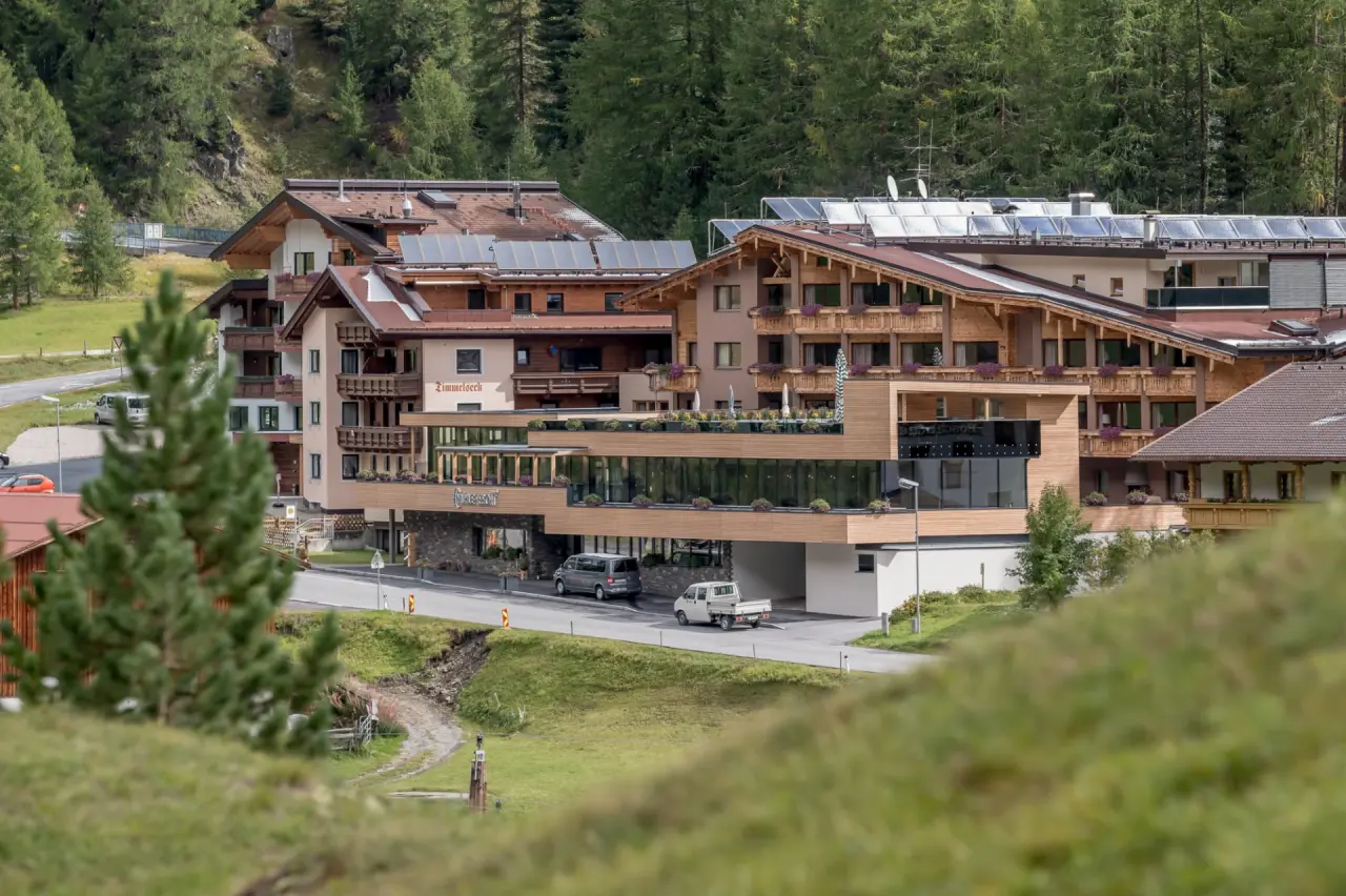 Aussenansicht des Mühle Resort 1900 in alpiner Landschaft, umgeben von grünen Wäldern und Bergen.