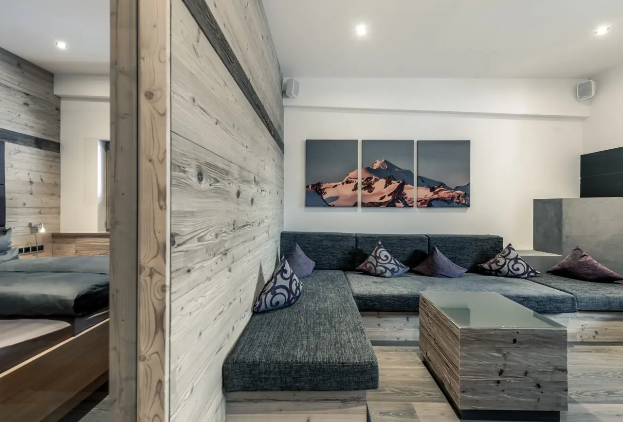 Gemütlicher Wohnbereich einer Suite im Mühle Resort 1900 mit Holzelementen, bequemer Sitzecke und Bergbildern.