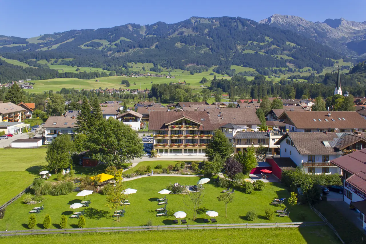 Luftaufnahme des Hotel Rosenstock mit weitläufigem Garten, Liegewiesen und Alpenpanorama im Hintergrund.