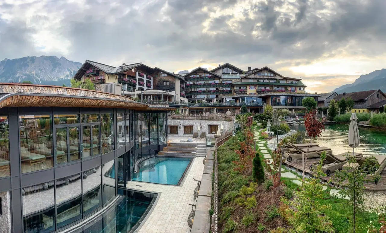 Grosszügige Aussenanlage des Wellnesshotel Engel mit modernem Spa-Bereich, Aussenpool und idyllischem Naturteich vor Bergpanorama.