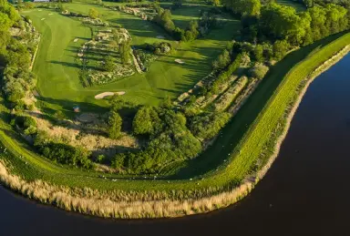 Luftaufnahme des weitläufigen Golfplatzes am Wasser des Hotel Breitenburg mit grünen Fairways und Bunkern.