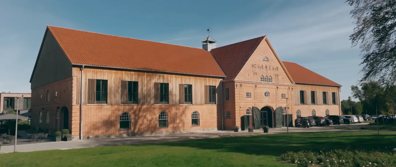 Historische Aussenansicht des Hotel Breitenburg mit rotem Ziegeldach, Backsteinfassade und gepflegten Gruenflaechen.