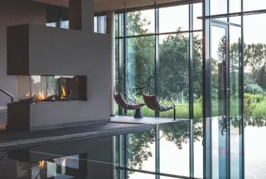 Moderner Innenpool mit Kamin und Panoramafenstern zum Garten im Wellnessbereich des Hotel Breitenburg.