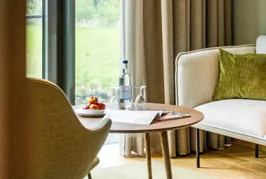 Gemütliche Sitzecke im Hotel Breitenburg mit frischem Wasser, Äpfeln und Magazin am Fenster mit Blick ins Grüne.
