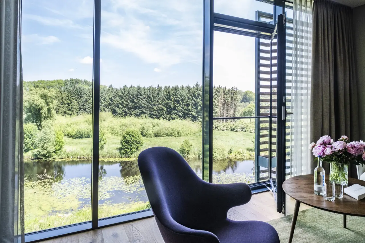Modernes Hotelzimmer im Hotel Breitenburg mit bodentiefen Fenstern und Blick auf Fluss und grüne Natur.