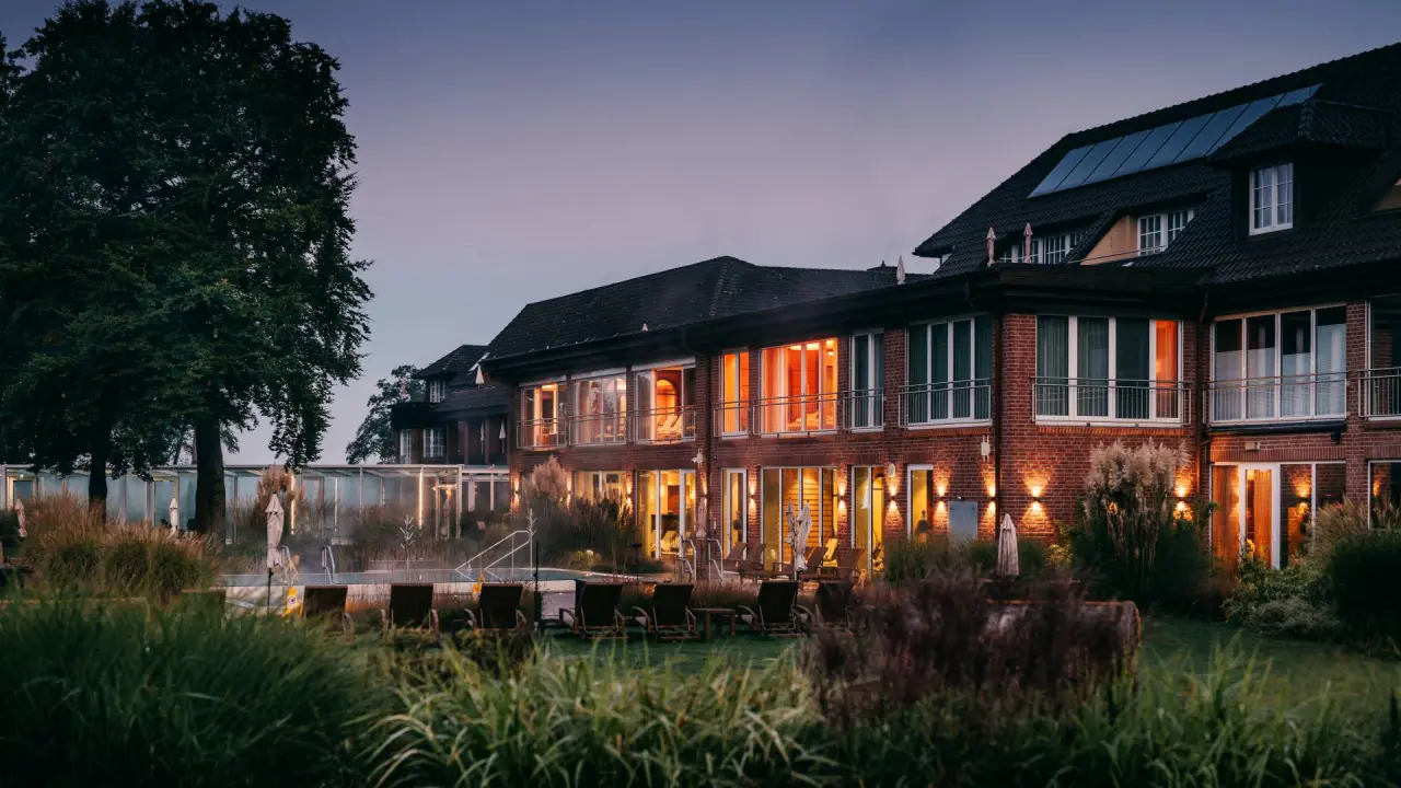 Romantik Hotel Jagdhaus Eiden bei Dämmerung mit beleuchteter Fassade und dampfendem Aussenpool im Gartenbereich.