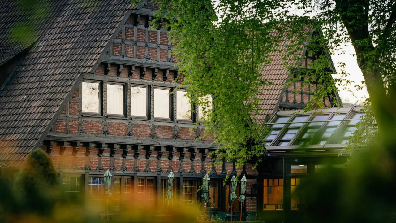 Teilansicht des traditionellen Romantik Hotel Jagdhaus Eiden mit Fachwerkfassade, Ziegeldach und modernem Glasanbau, umgeben von Grün.