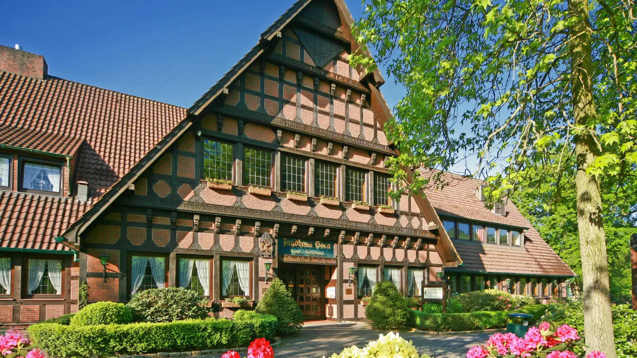 Romantik Hotel Jagdhaus Eiden: Traditionelles Fachwerkhaus mit einladendem Eingang, umgeben von grüner Bepflanzung und bunten Blumen.