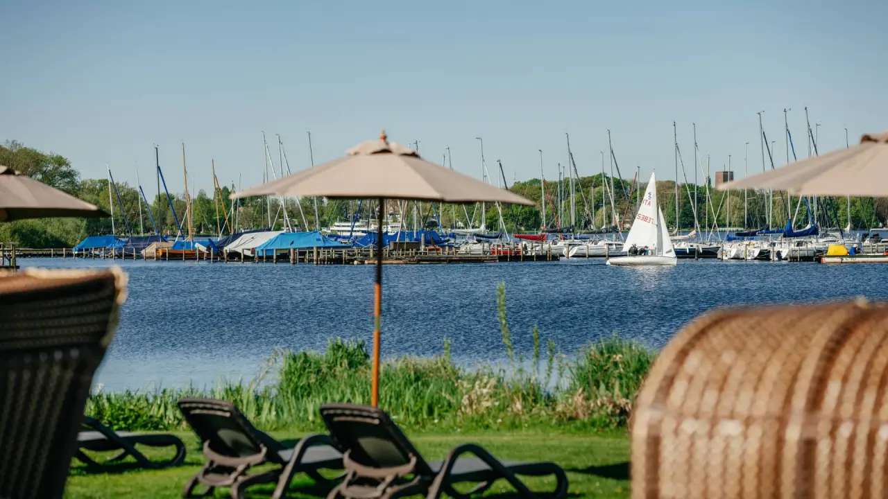 Sonnenliegen und Sonnenschirme am Ufer des Zwischenahner Meeres mit Blick auf den Yachthafen im Romantik Hotel Jagdhaus Eiden.