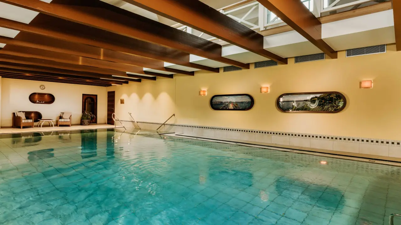 Grosszügiger Innenpool mit warmem Ambiente und Holzbalkendecke im Romantik Hotel Jagdhaus Eiden.