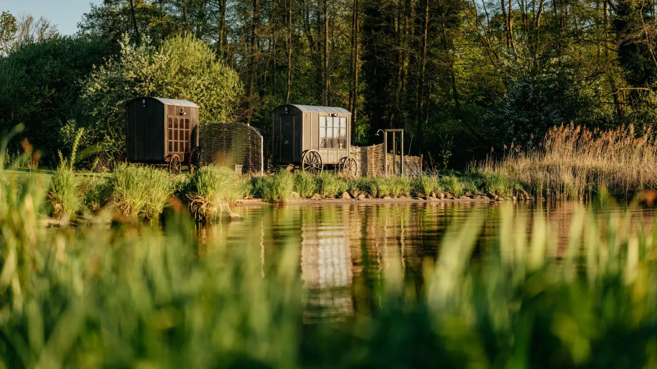 Zwei private Saunawagen am idyllischen Seeufer des Romantik Hotel Jagdhaus Eiden, eingebettet in grüne Natur und Schilf.