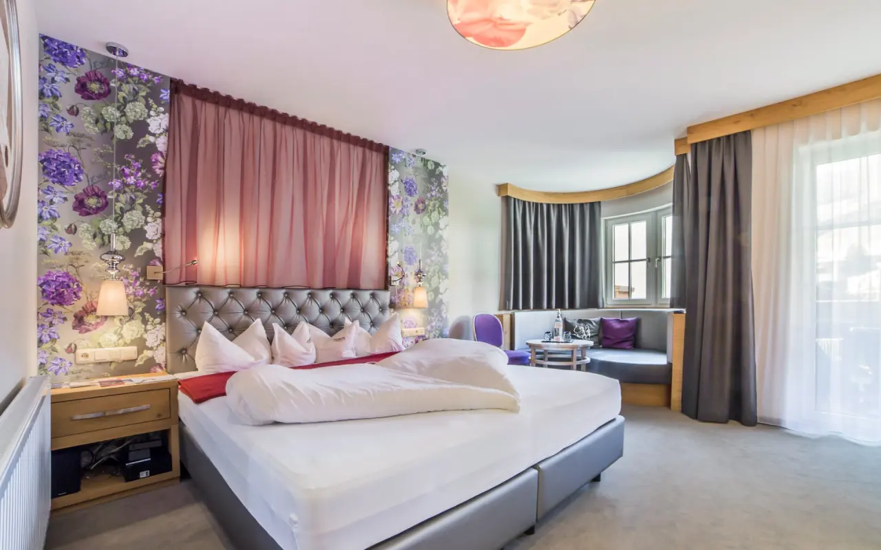 Gemütliches Doppelzimmer im mein romantisches Hotel Garni Toalstock mit floraler Tapete, bequemen Bett und Sitzbereich.