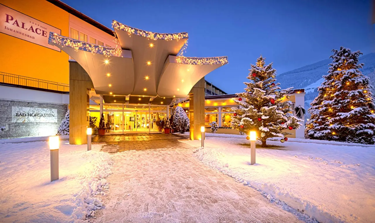 Festlich beleuchteter Hoteleingang des Johannesbad Hotel Palace in Bad Hofgastein im Winter mit Schnee und Weihnachtsbäumen.
