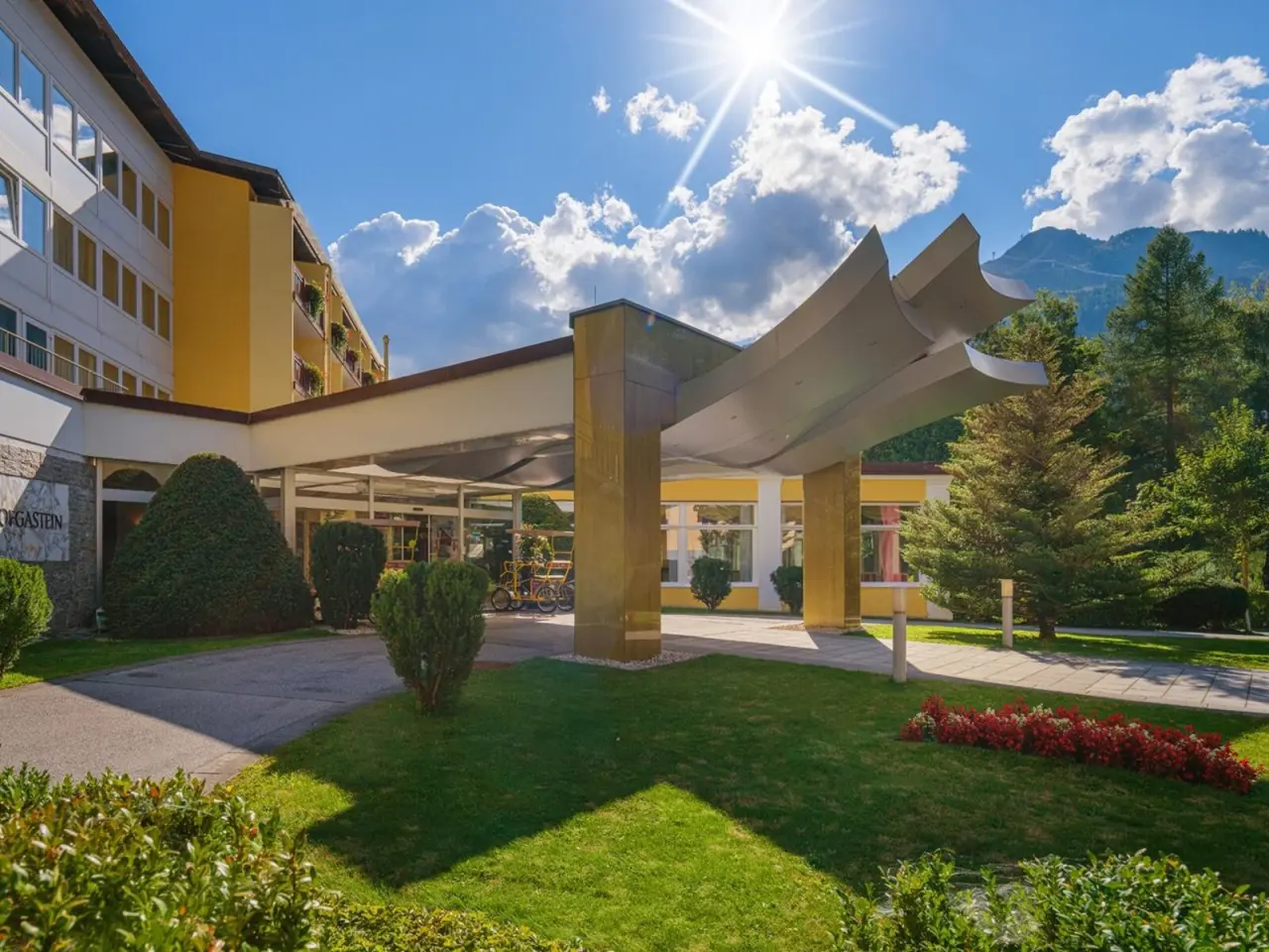 Sonniger Eingangsbereich des Johannesbad Hotel Palace mit moderner Architektur und Alpenpanorama.