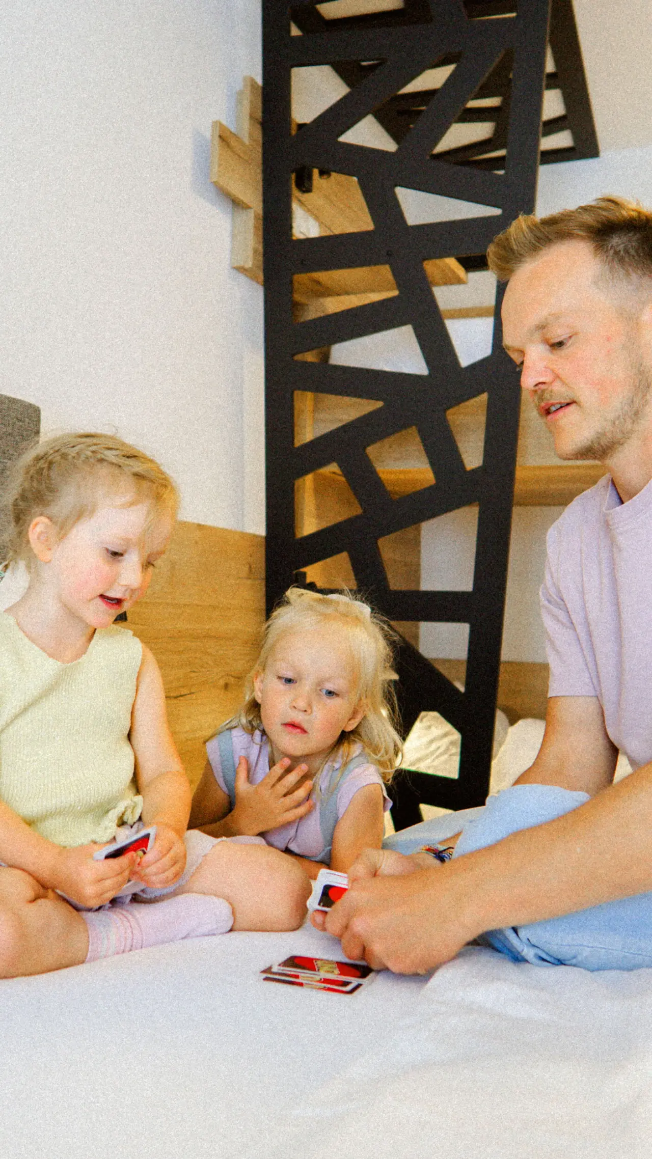 Familie spielt Karten im gemütlichen Hotelzimmer des BergBuddies. Vater und zwei Kinder genießen gemeinsame Zeit auf dem Bett.