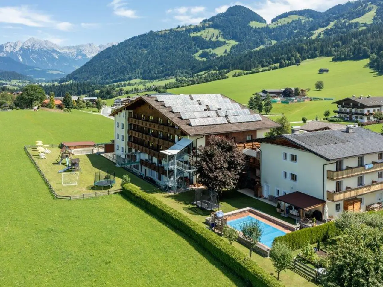 Aussenansicht des Sporthotel Tirolerhof mit Pool, Spielplatz und Alpenpanorama in den Bergen.