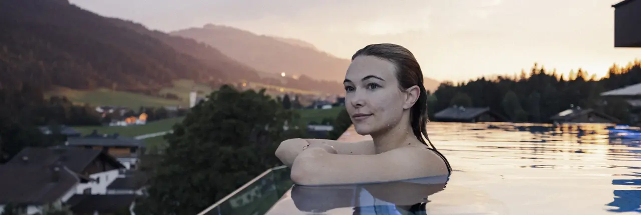 Entspannte Frau im Infinity Pool des Wellnessresort Seiwald bei Sonnenuntergang mit Alpenpanorama.