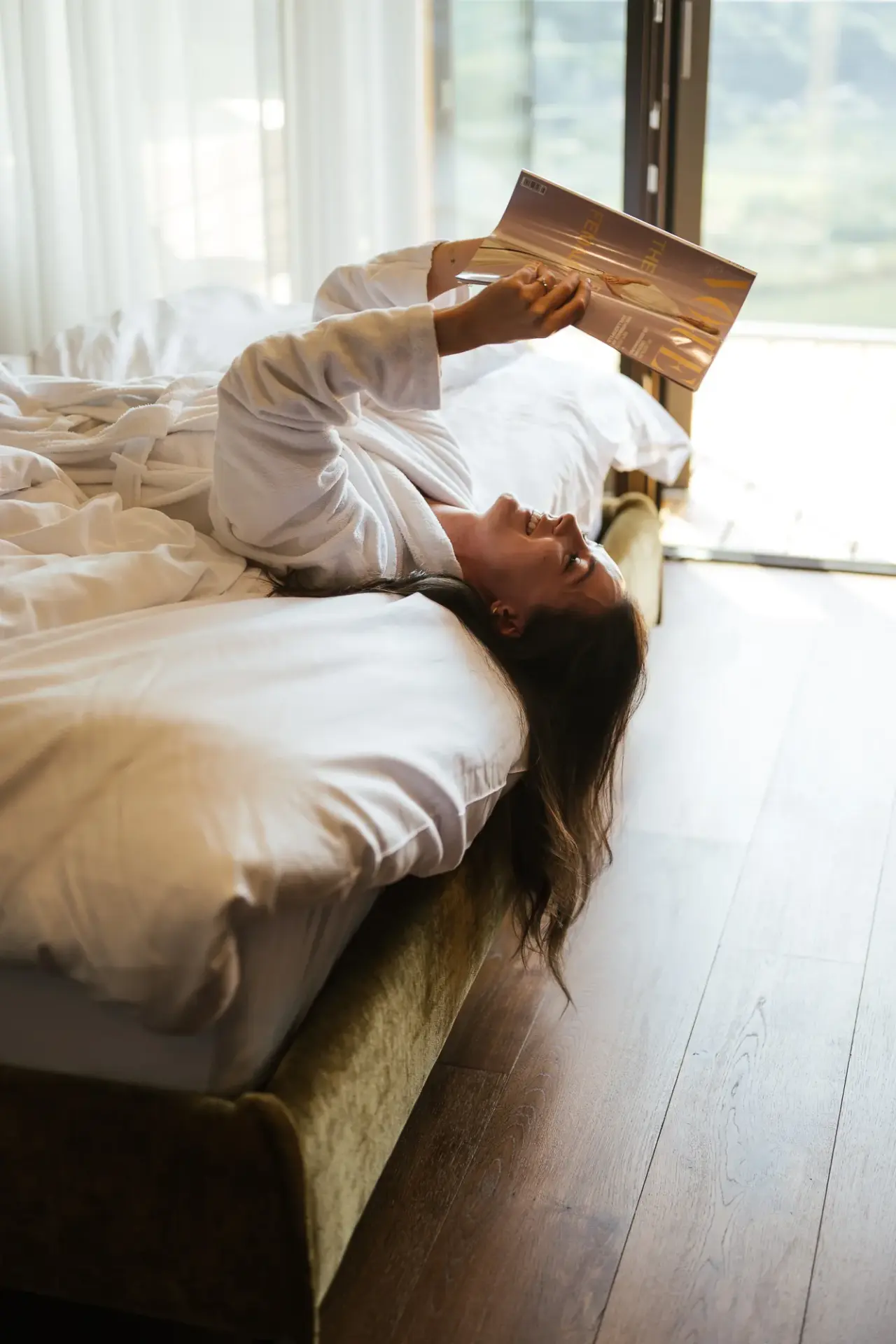 Feel Good Resort Johannis in Dorf Tirol – Gast im Bademantel entspannt lesend auf dem Hotelbett | Wellnesshotel Südtirol