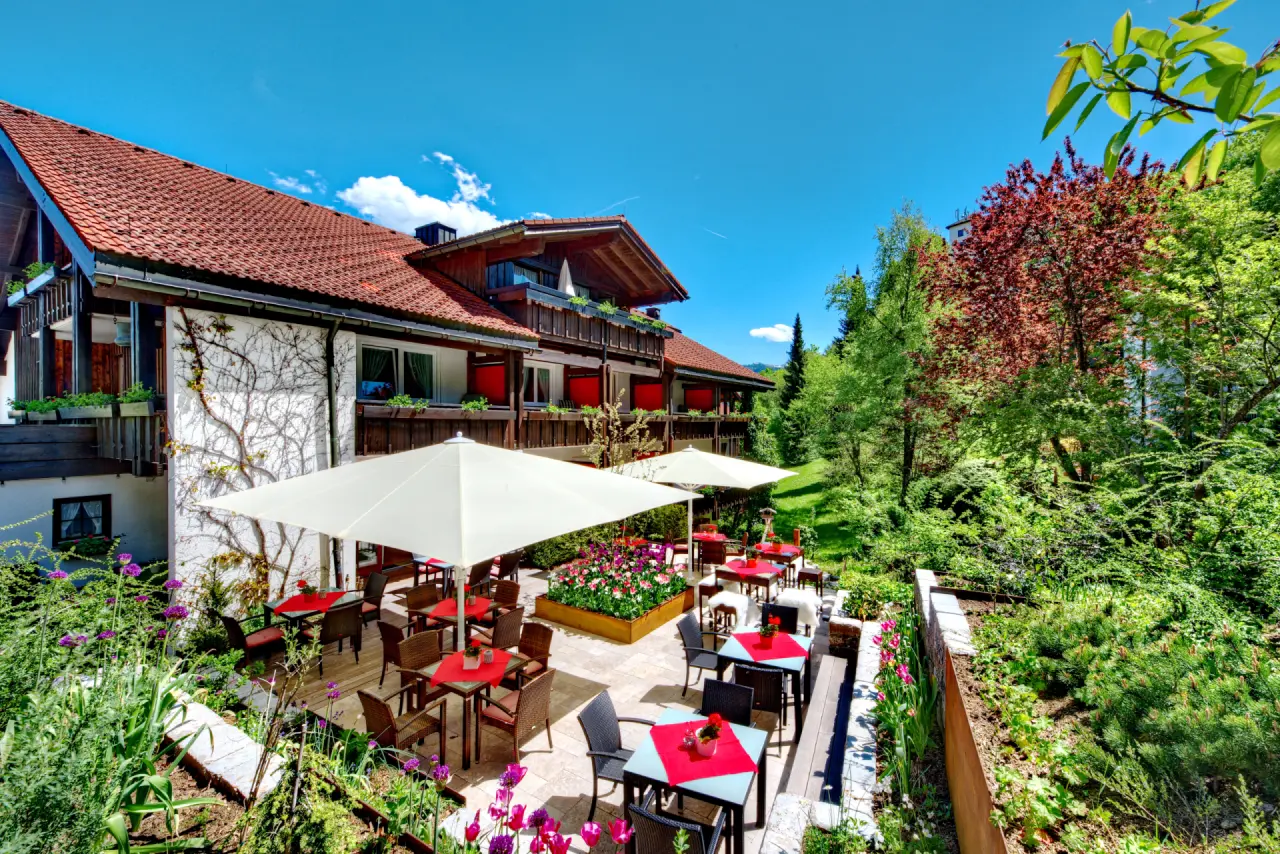 Sonnige Gartenterrasse des DIANA Naturpark Hotels mit blühenden Blumen und einladenden Sitzgelegenheiten im Grünen.