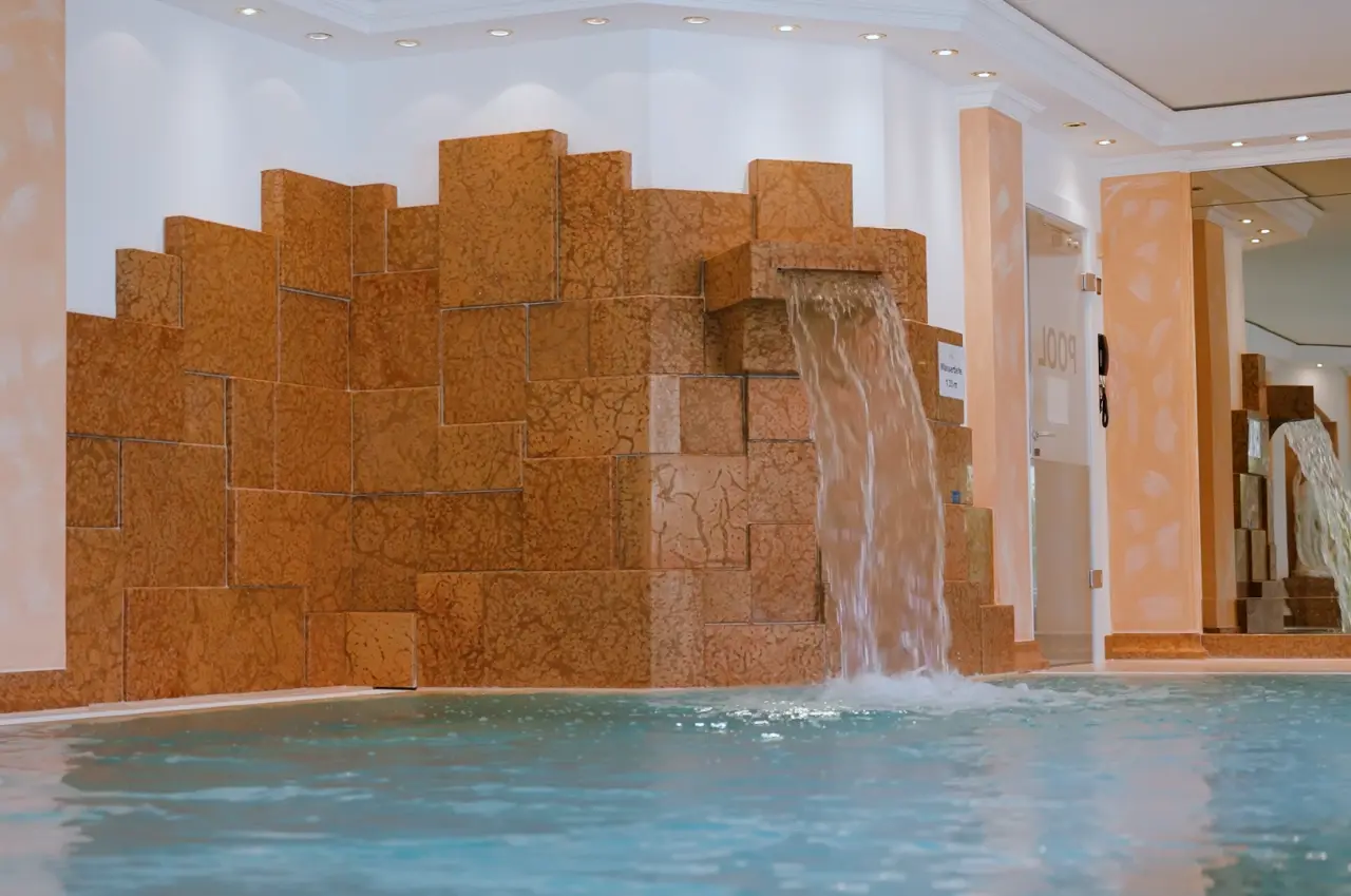Innenpool mit Wasserfall und dekorativer Steinwand im Wellnessbereich des DIANA Naturpark Hotels.