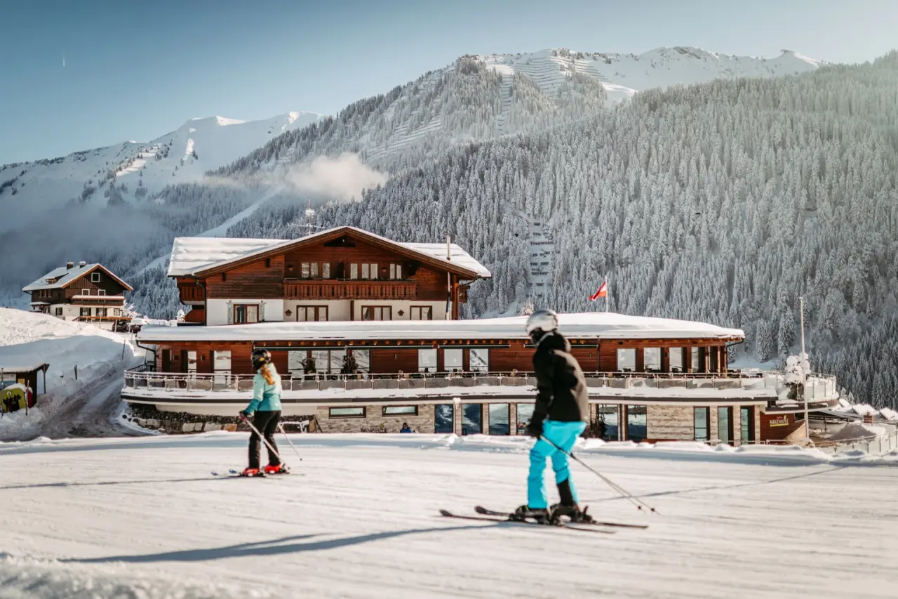 Hotel Birkenhöhe im Winter, direkt an der Skipiste mit Skifahrern und majestätischen verschneiten Bergen. Ideal für Wellness & Skiurlaub.