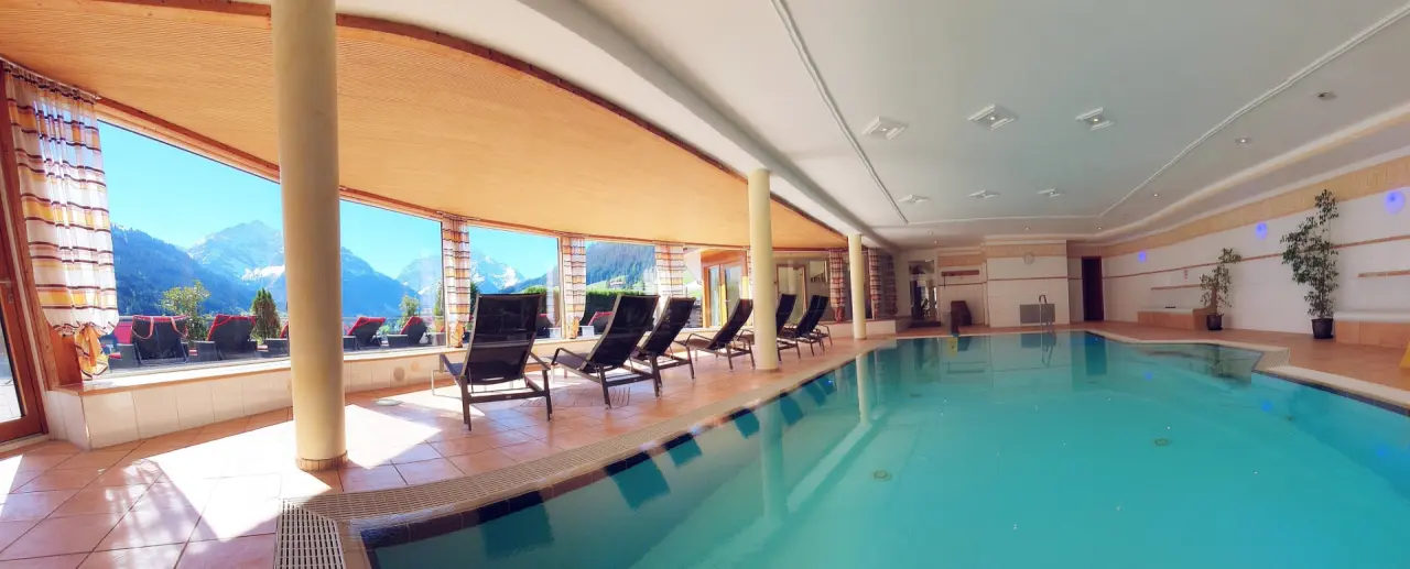 Grosszügiger Innenpool mit Panoramablick auf die Alpen und Liegestühlen im Wellnessbereich des Hotel Birkenhöhe.