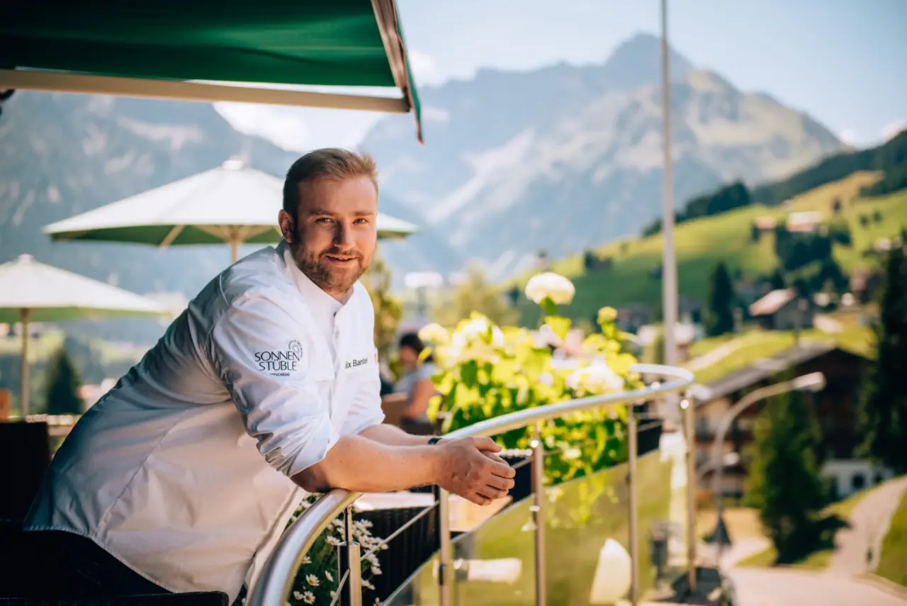 Lachender Küchenchef Felix Bantel der Sonnen Stuble auf der Sonnenterrasse des Hotel Birkenhöhe mit Alpenpanorama.
