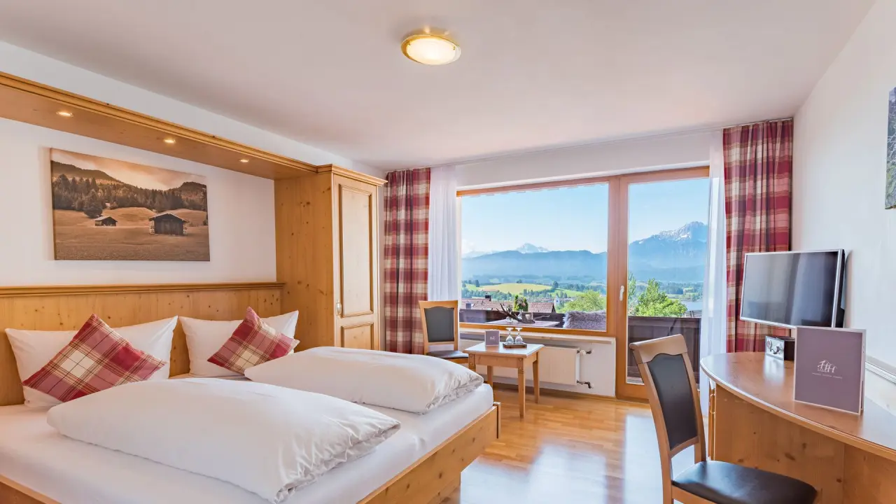 Gemütliches Doppelzimmer im Hartung’s Hoteldorf mit Balkon und Panoramablick auf die Allgäuer Alpen und grüne Landschaft.