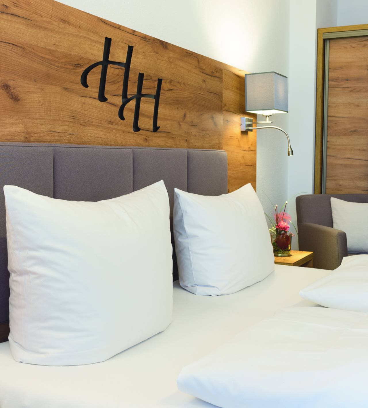 Hartung’s Hoteldorf in Füssen – Detailansicht des Hotelbettes mit Logo an der Holzwand | Wellnesshotel Allgäu