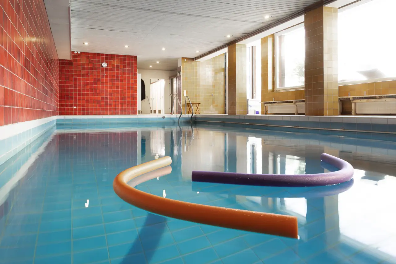 Innenpool im Parkhotel Hitzacker mit blauen Fliesen, roten Wänden und großen Fenstern für entspannte Schwimmstunden.