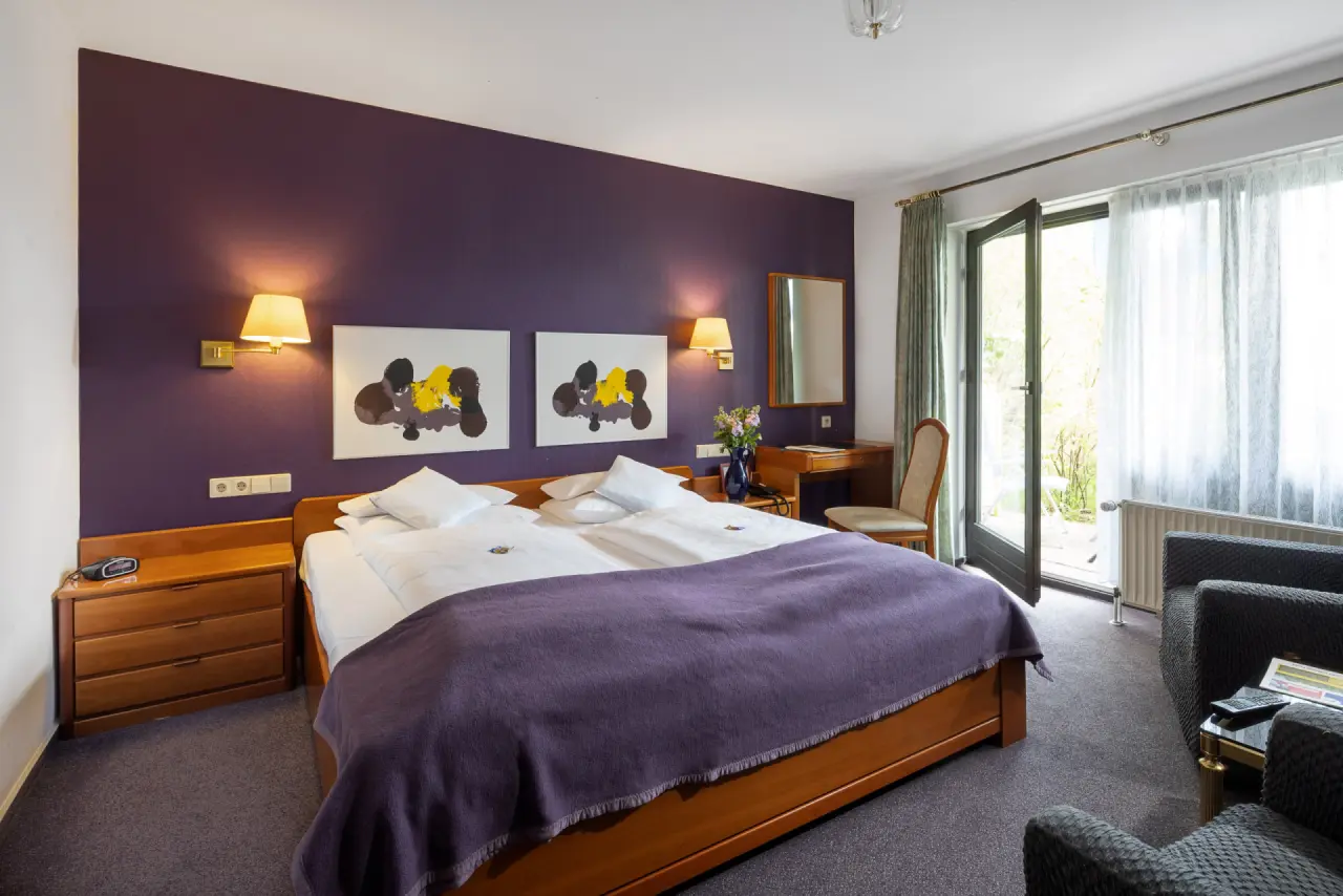 Gemütliches Doppelzimmer mit lila Wand, Holzbett und Balkon im Parkhotel Hitzacker.