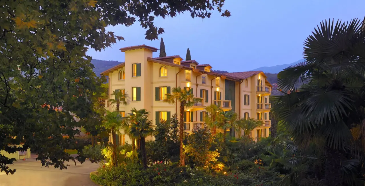 Du Lac et Du Parc Grand Resort in Riva del Garda – Beleuchtete Außenansicht mit Palmen bei Dämmerung | Wellnesshotel Gardasee