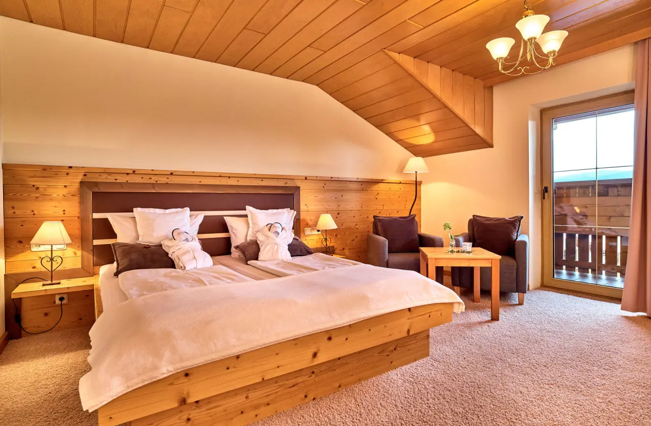 Gemütliches Doppelzimmer mit Holzelementen, Balkon und Bademänteln im Wellnesshotel St. Gunther.