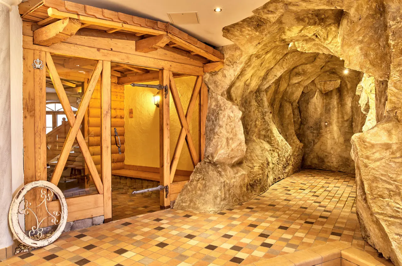 Rustikaler Sauna-Eingang aus Holz und Felsengrotte mit Dusche im Wellnessbereich des Wellnesshotel St. Gunther.