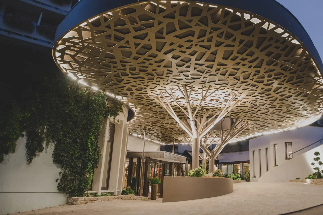 Modernes Eingangsportal mit beleuchtetem Blätterdach und Kletterpflanzen am Kunzmann's Hotel | Spa