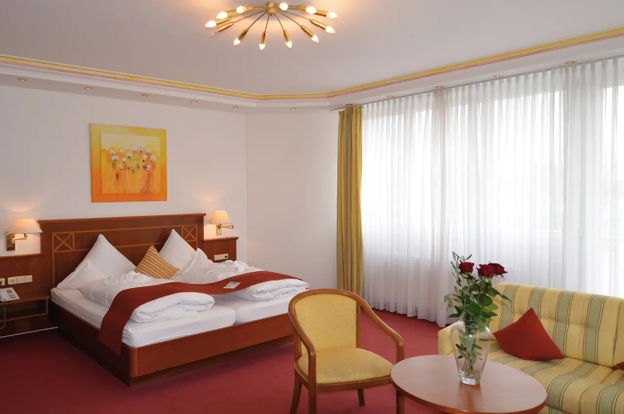 Gemütliches Doppelzimmer im ANGERHOF Kur- und Sporthotel mit Doppelbett, Sitzbereich und Fenster.