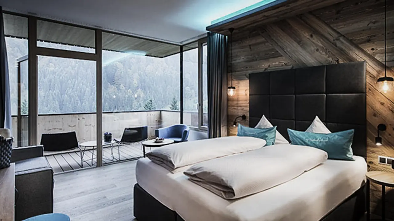 Geräumiges Hotelzimmer im Wellnesshotel Walserhof mit Doppelbett, Holzwänden und Balkon mit Bergblick.