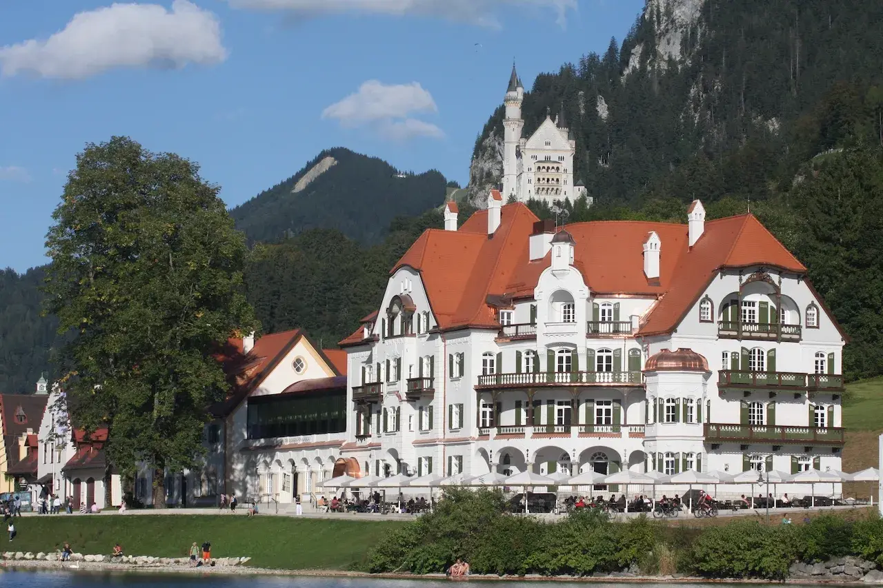 AMERON Neuschwanstein Alpsee Resort & Spa mit Blick auf den Alpsee und Schloss Neuschwanstein im Hintergrund.